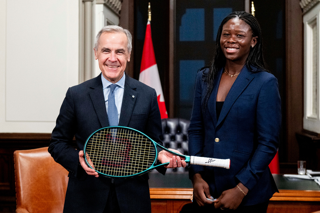 Canada Prime Minister Mark Carney, left, and tennis champion Victoria Mboko are pictured as Carney holds Mboko's tennis racket used to win the 2025 National Bank Open in Montreal during a meeting on Parliament Hill in Ottawa, on Wednesday, Dec. 3, 2025. (Spencer Colby/The Canadian Press via AP)