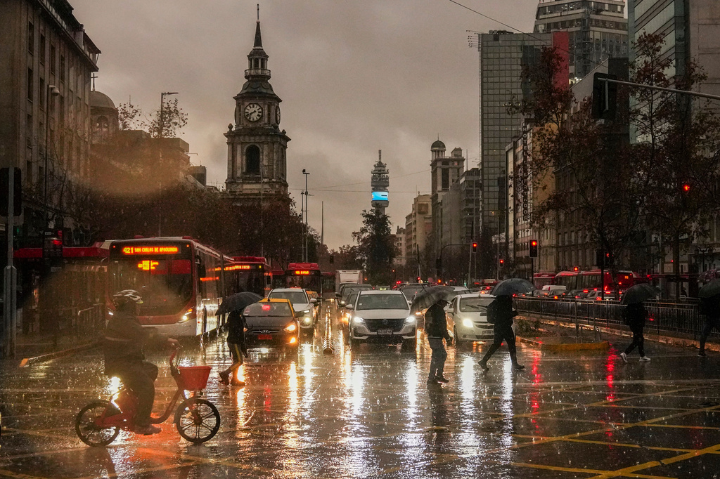 People cross Alameda Bernardo O'Higgins Avenue during a rainstorm in Santiago, Chile, early Monday, July 20, 2026. (AP Photo/Esteban Felix)