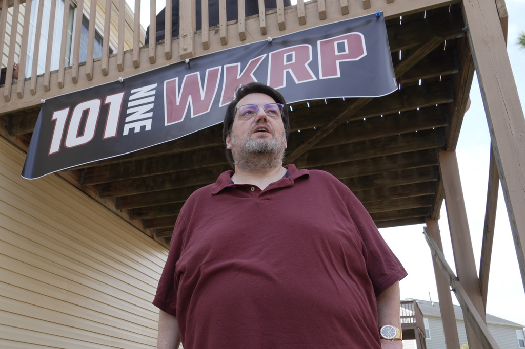 D.P. McIntire stands beneath a WKRP banner in the backyard of his home in Raleigh, N.C., on Thursday, April 2, 2026. (AP Photo/Allen G. Breed)