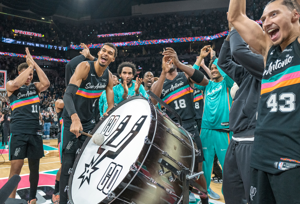 San Antonio Spurs forward Victor Wembanyama (1) hits on a drum as he and teammates celebrate with the Spurs fans after defeating the Oklahoma Thunder in an NBA basketball game in San Antonio, Tuesday, Dec. 23, 2025. (AP Photo/Rodolfo Gonzalez)