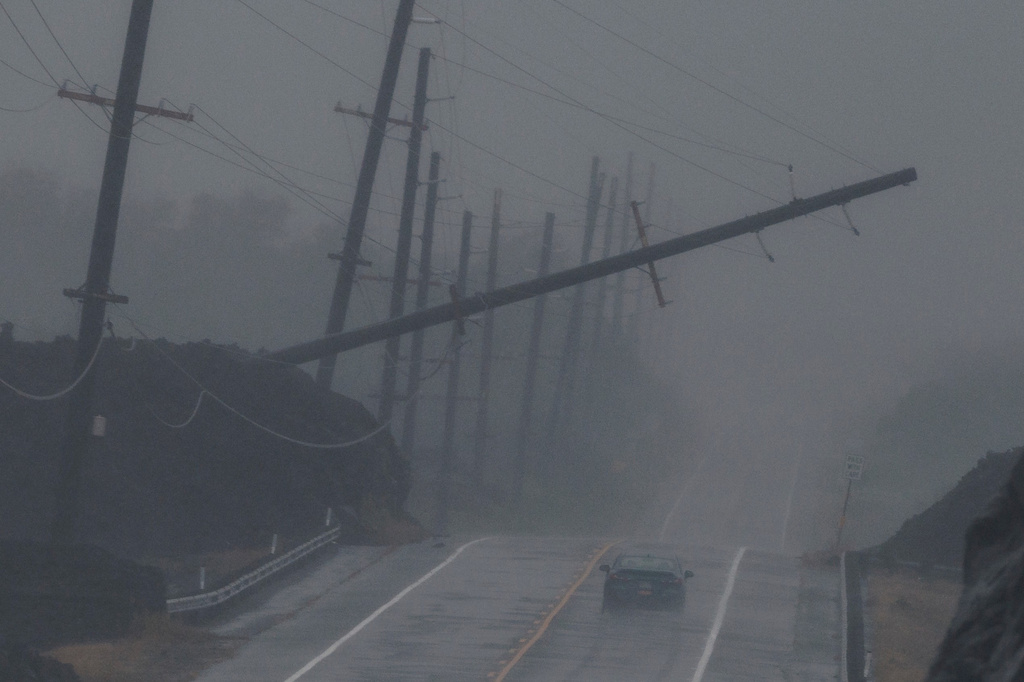 A vehicle drives near a downed utility pole dangling above Mamalahoa Highway during Hurricane Lala near Ocean View, Hawaii, Saturday, Aug. 15, 2026. (Stephen Lam/San Francisco Chronicle via AP)