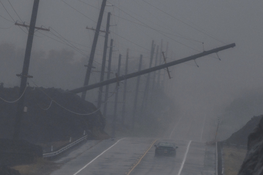 A vehicle drives near a downed utility pole dangling above Mamalahoa Highway during Hurricane Lala near Ocean View, Hawaii, Saturday, Aug. 15, 2026. (Stephen Lam/San Francisco Chronicle via AP)