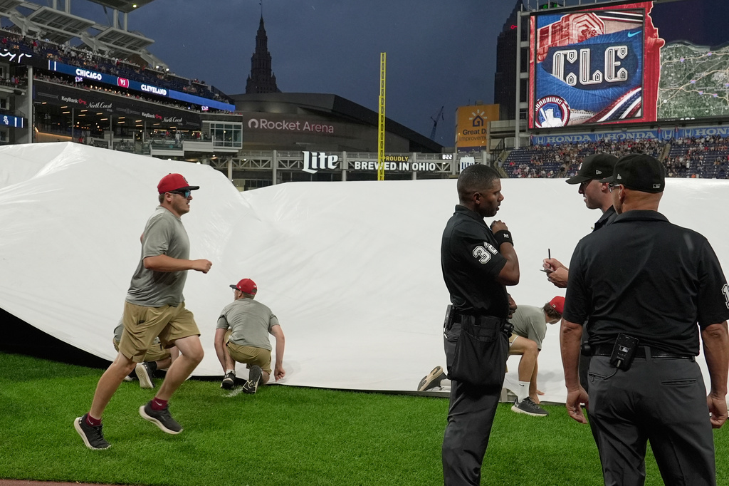 Umpires Edwin Moscoso (32), Nic Lentz, center, and Carapazza, right, talks near first base as the grounds crew covers the field with a tarp as a storm moves into Progressive Field in the fifth inning of a baseball game between the Chicago White Sox and the Cleveland Guardiansin Cleveland, Friday, July 3, 2026. (AP Photo/Sue Ogrocki)