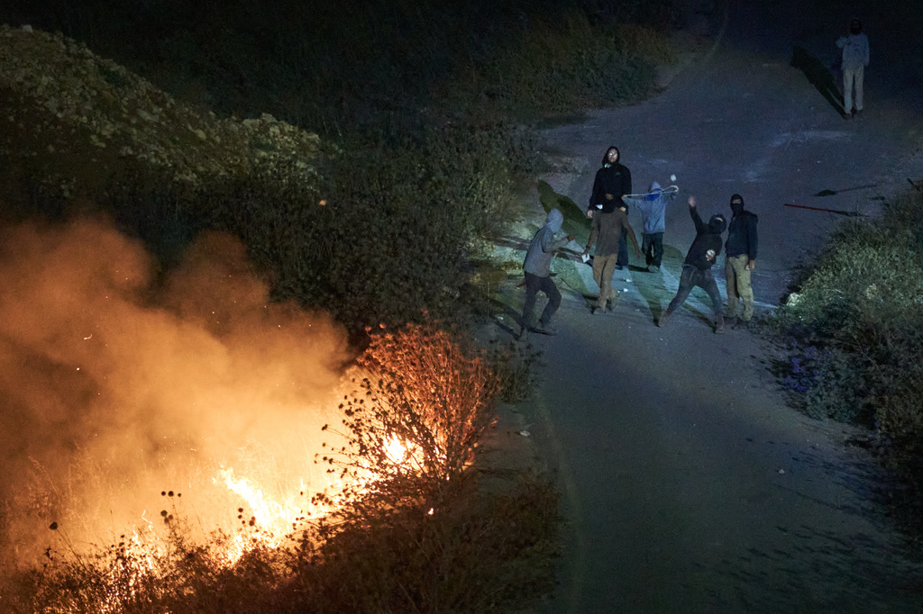 Israeli settlers throw stones as brush burns along a roadside after Palestinians set it ablaze to prevent the settlers from approaching the West Bank village of Sinjil, Friday, July 17, 2026. (AP Photo/Leo Correa)