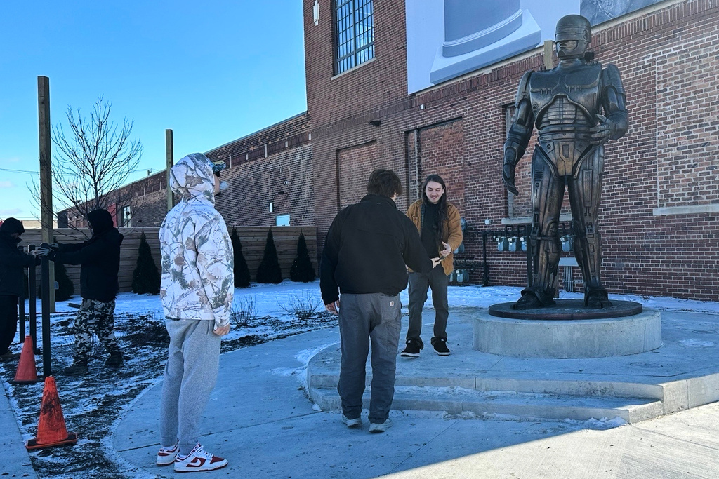 People pose for photos with a RoboCop statue that stands outside a business in Detroit's Eastern Market area, Thursday, Dec. 4, 2025. (AP Photo/Mike Householder)