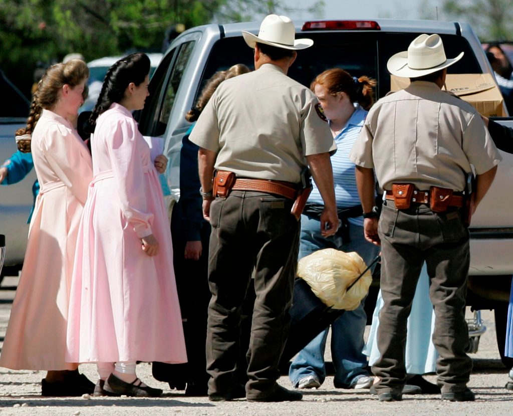 FILE - Members of the Fundamentalist Church of Jesus Christ of Latter Day Saints, left, walk toward a waiting charter bus as Schleicher County Sheriffs deputies help provide security, Sunday, April 6, 2008, in Eldorado, Texas. The two and other members of their church were being relocated to temporary housing in San Angelo, Texas. (AP Photo/Tony Gutierrez, File)