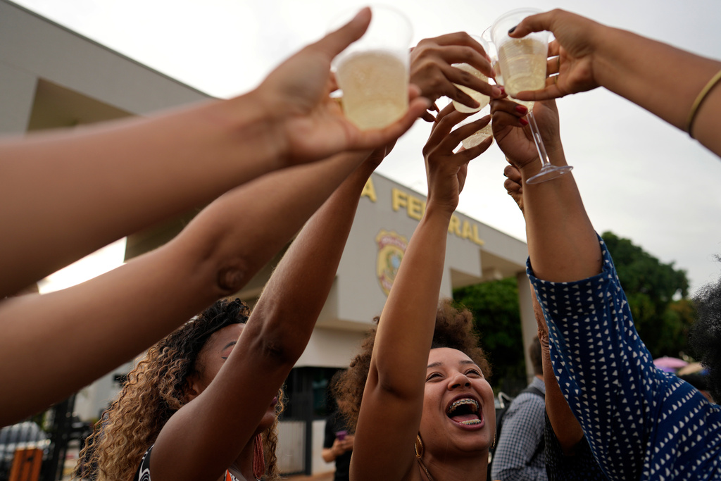 Detractors of former President Jair Bolsonaro hold up glasses of champagne, celebrating his sentence for leading a coup attempt, outside the federal police headquarters, where he is under arrest in Brasilia, Brazil, Tuesday, Nov. 25, 2025. (AP Photo/Eraldo Peres)