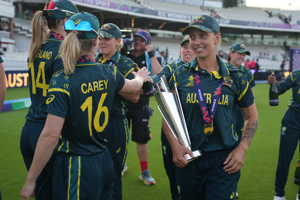 Australia's Ashleigh Gardner, carries the trophy as teammates celebrate after winning the Women's T20 Cricket World Cup final between England and Australia in London, Sunday, July 5, 2026. (AP Photo/Alastair Grant)