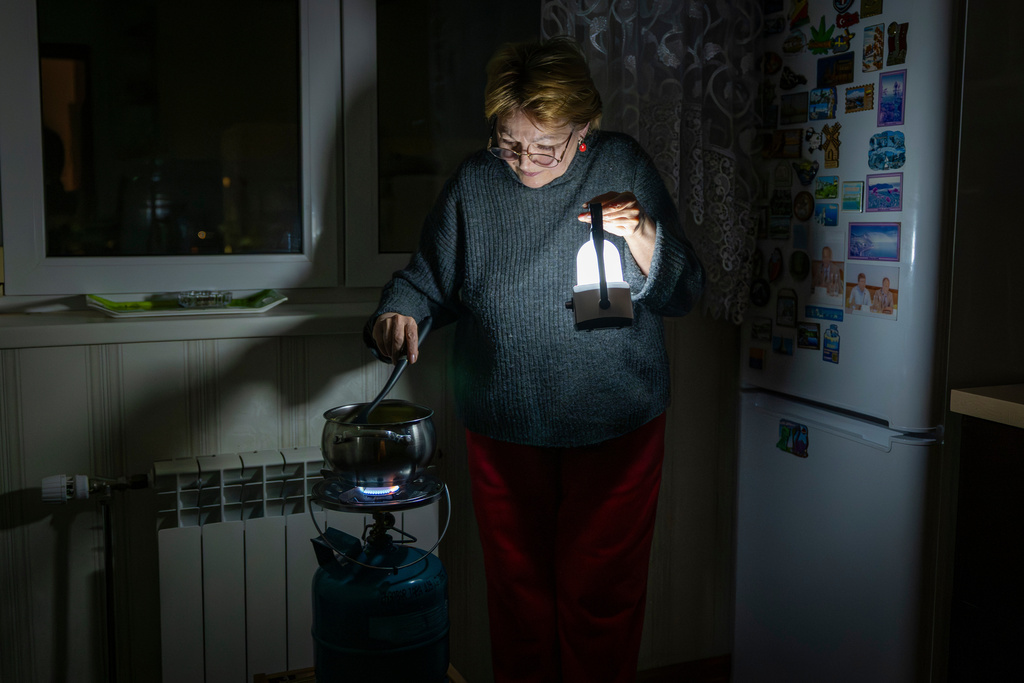 Olena Janchuk's mother cooks food on a gas burner by lantern light during a blackout in Kyiv following Russian attacks on energy infrastructure in Kyiv, Ukraine, Tuesday, Jan. 20, 2026. (AP Photo/Dan Bashakov)