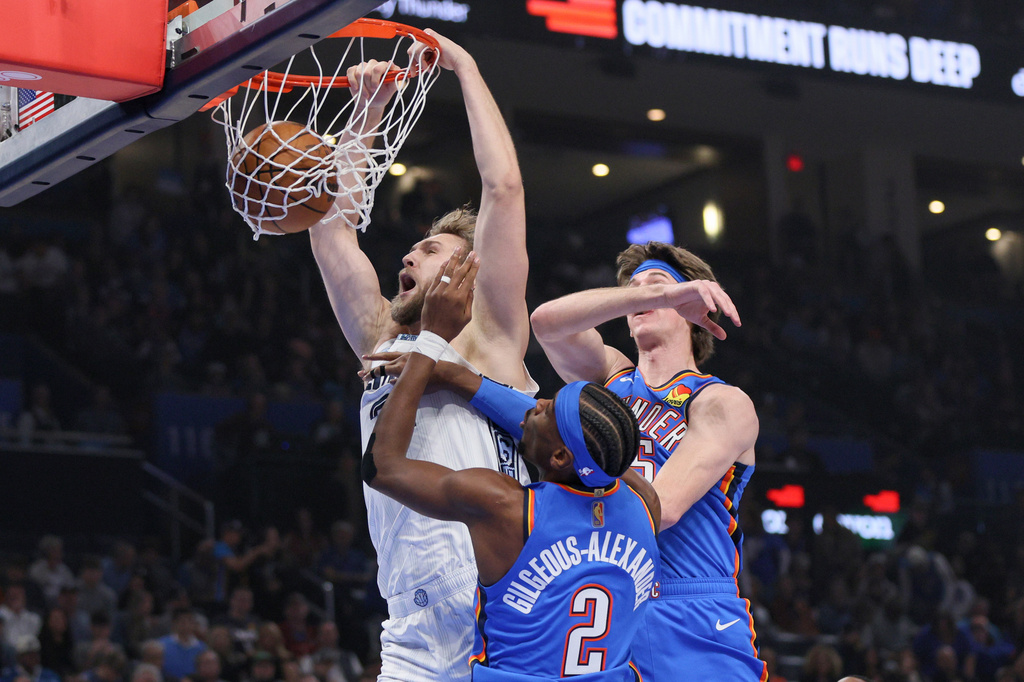Memphis Grizzlies center Jock Landale, left, dunks next to Oklahoma City Thunder guard Shai Gilgeous-Alexander (2) and center Branden Carlson, top right, during the first half of an NBA basketball game Monday, Dec. 22, 2025, in Oklahoma City. (AP Photo/Nate Billings)
