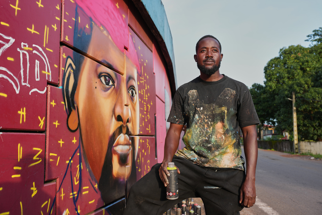 Graffiti artist Omar Diaw poses beside his mural depicting Guinea's President Mamadi Doumbouya on a street wall in Conakry, Guinea, Saturday, Sep. 20, 2025. (AP Photo/Misper Apawu)