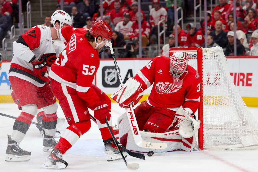 Detroit Red Wings goaltender John Gibson, right, saves a shot as Red Wings defenseman Moritz Seider (53) guards against Carolina Hurricanes right wing Andrei Svechnikov, left, during the first period of an NHL hockey game Monday, Jan. 12, 2026, in Detroit. (AP Photo/Ryan Sun)