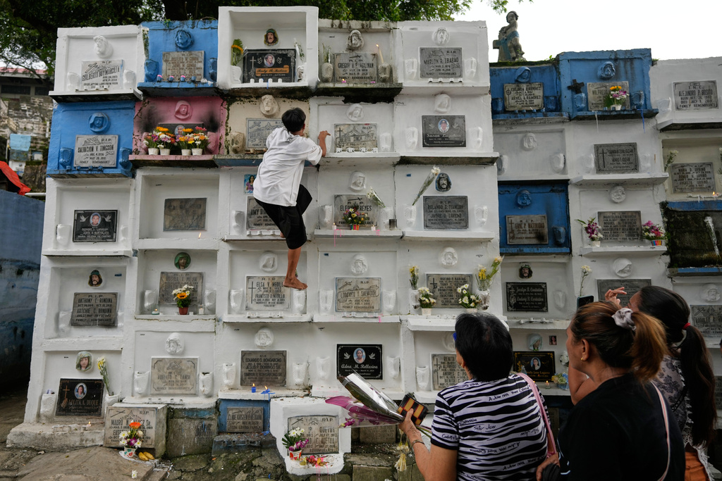 A man climbs apartment-type tombs at the hillside Barangka public cemetery in Marikina city, Philippines as people visit their loved ones during All Saints Day on Saturday, Nov. 1, 2025. (AP Photo/Aaron Favila)