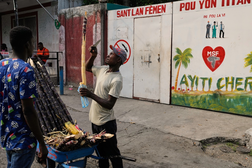 A vendor sells sugarcane next to the entrance of the Doctors Without Borders (MSF) clinic in Port-au-Prince, Haiti, Wednesday, Oct. 15, 2025, after the organization announced the facility’s closure due to ongoing violence. (AP Photo/Odelyn Joseph)