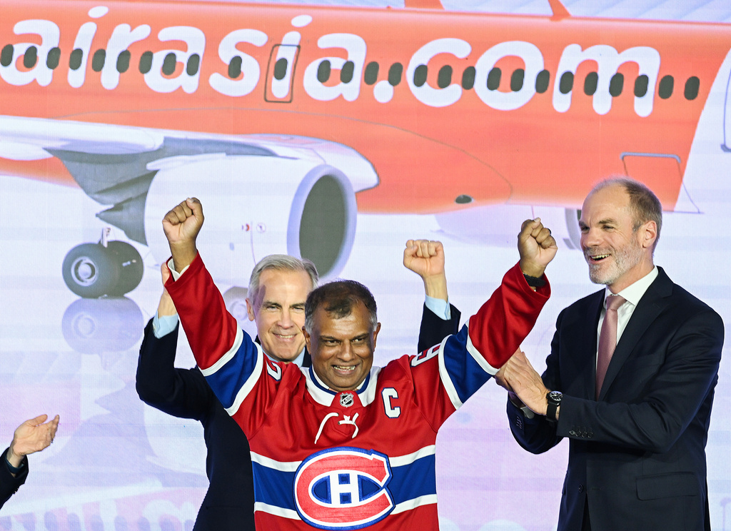 Canada's Prime Minister Mark Carney, left, and Lars Wagner, CEO, Airbus Commercial Aircraft, right, cheer on AirAsia CEO Tony Fernandes, centre, during an event at the Airbus A220 Delivery Center in Mirabel, Que., Wednesday, May 6, 2026, where AirAsia placed a landmark order for 150 Airbus A220 aircraft. (Graham Hughes/The Canadian Press via AP)