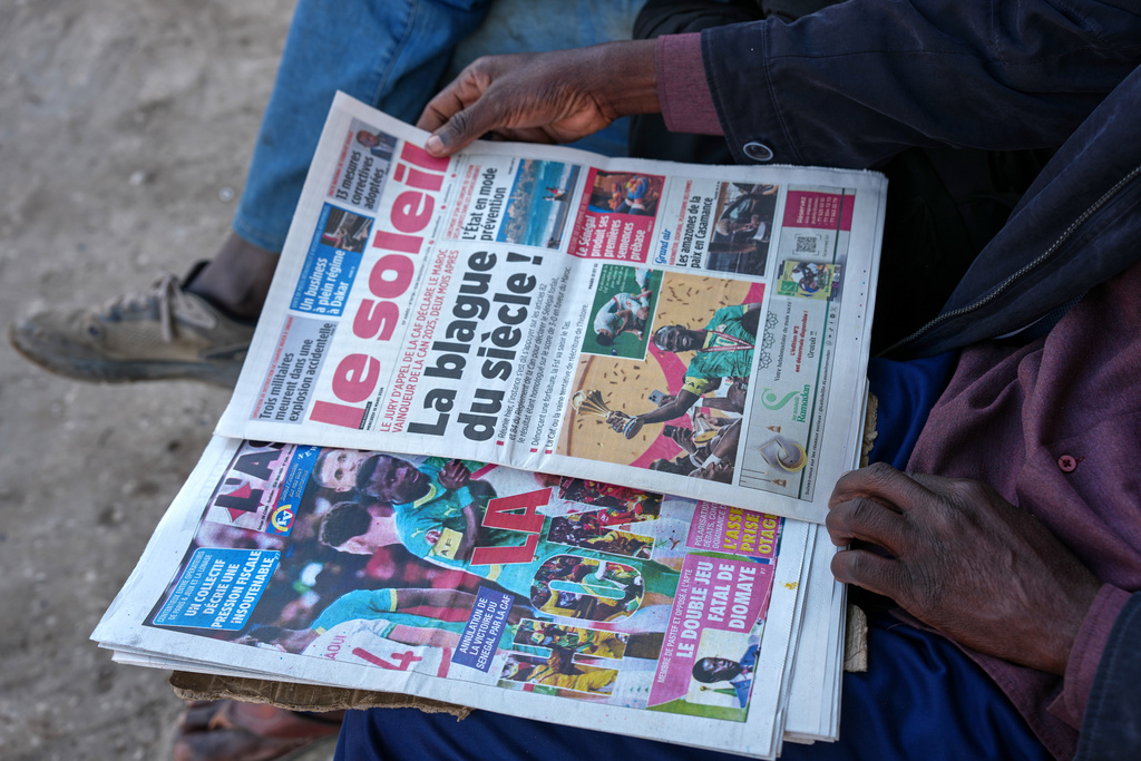 People read newspapers reporting on the Confederation of African Football decision stripping the Senegal national football team of their Africa Cup of Nations title and awarding it to Morocco national football team in Dakar, Senegal, Wednesday, March 18, 2026. (AP Photo/Misper Apawu)