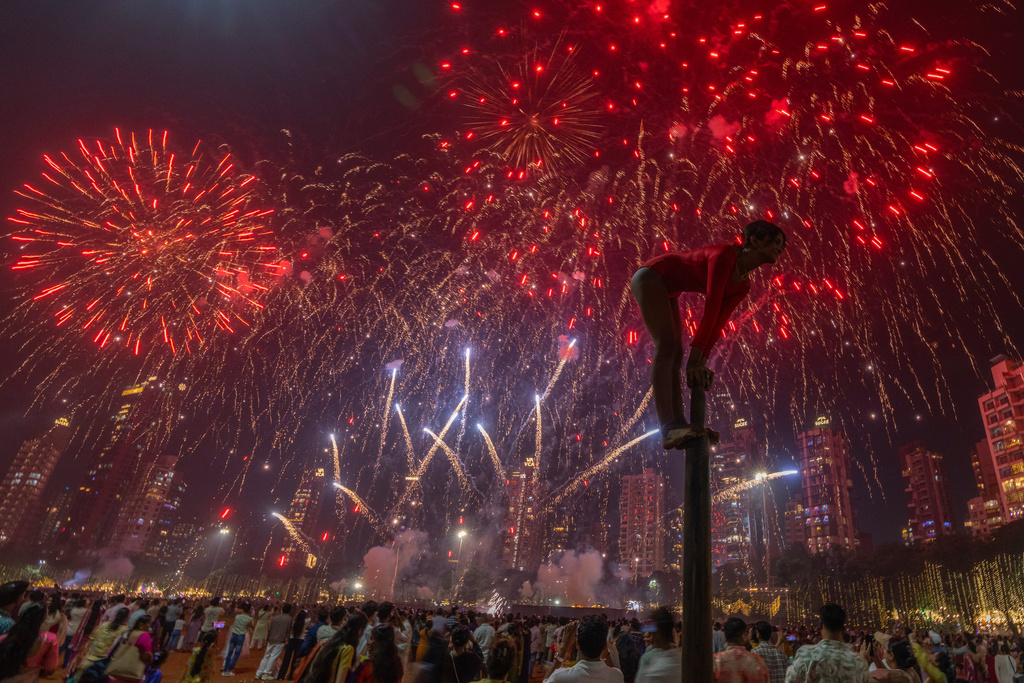 A girl performs on a mallakhamb pole as fireworks light up the sky during the Diwali festival of lights in Mumbai, India, on Monday, Oct. 20, 2025. (AP Photo/Rafiq Maqbool)