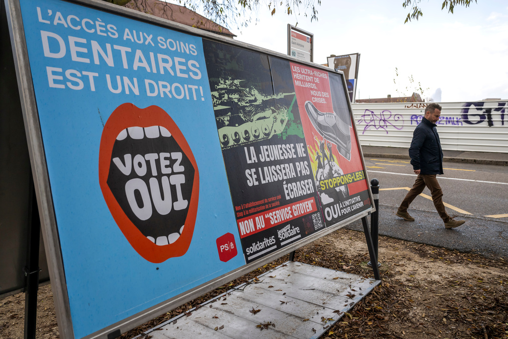 A person walks past referendum posters of political parties and associations as Swiss voters are casting ballots to decide whether women, like men, must do national service in the military, civil protection teams or in other forms, in Geneva, Switzerland, on Nov. 26, 2025. (Martial Trezzini/Keystone via AP)