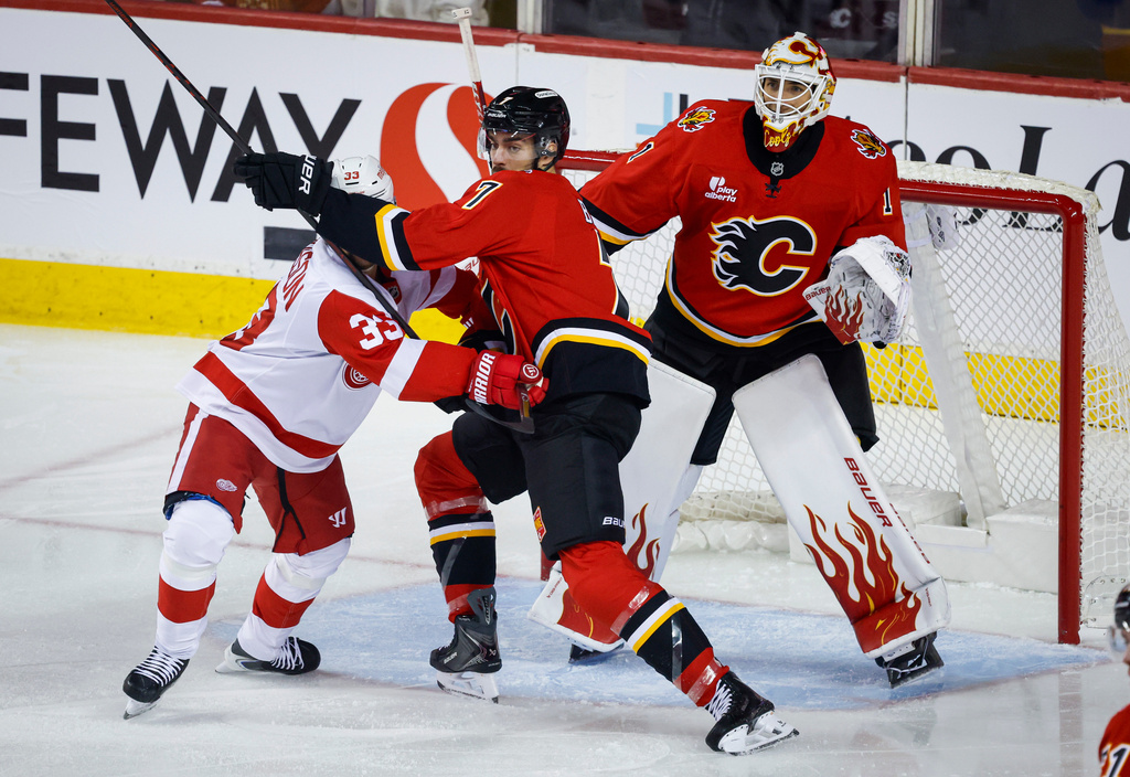 Detroit Red Wings' Viktor Arvidsson, left, is checked by Calgary Flames' Kevin Bahl, center, as goalie Devin Cooley follows the play during the first period of an NHL hockey game in Calgary, Alberta, Saturday, Oct. 24, 2026.(Jeff McIntosh/The Canadian Press via AP)