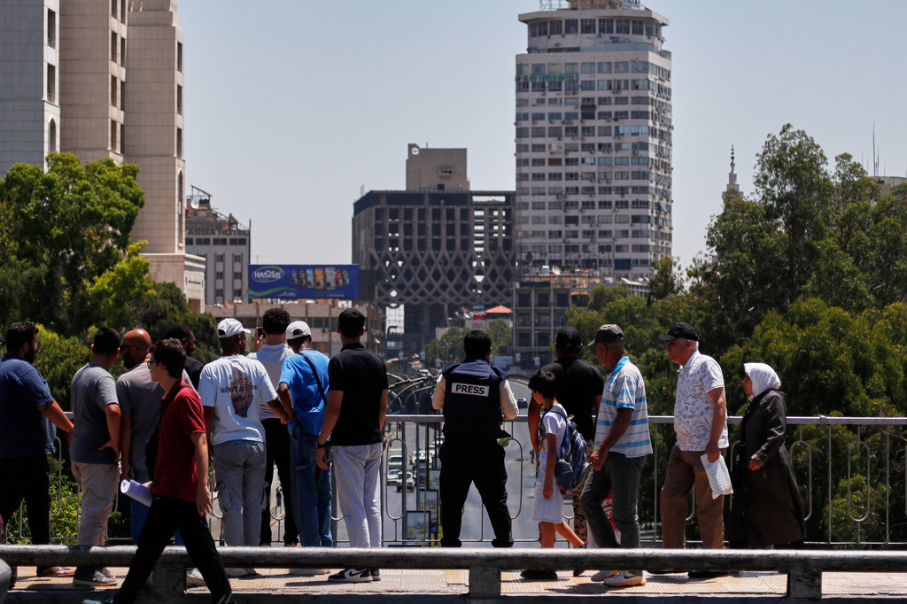 Onlookers and journalists watch from a bridge toward the area near the Four Seasons Hotel after two explosions rocked the site earlier while Syrian President Ahmad al-Sharaa was meeting French President Emmanuel Macron at the presidential palace in Damascus, Syria, Tuesday, July 7, 2026. (AP Photo/Omar Sanadiki)
