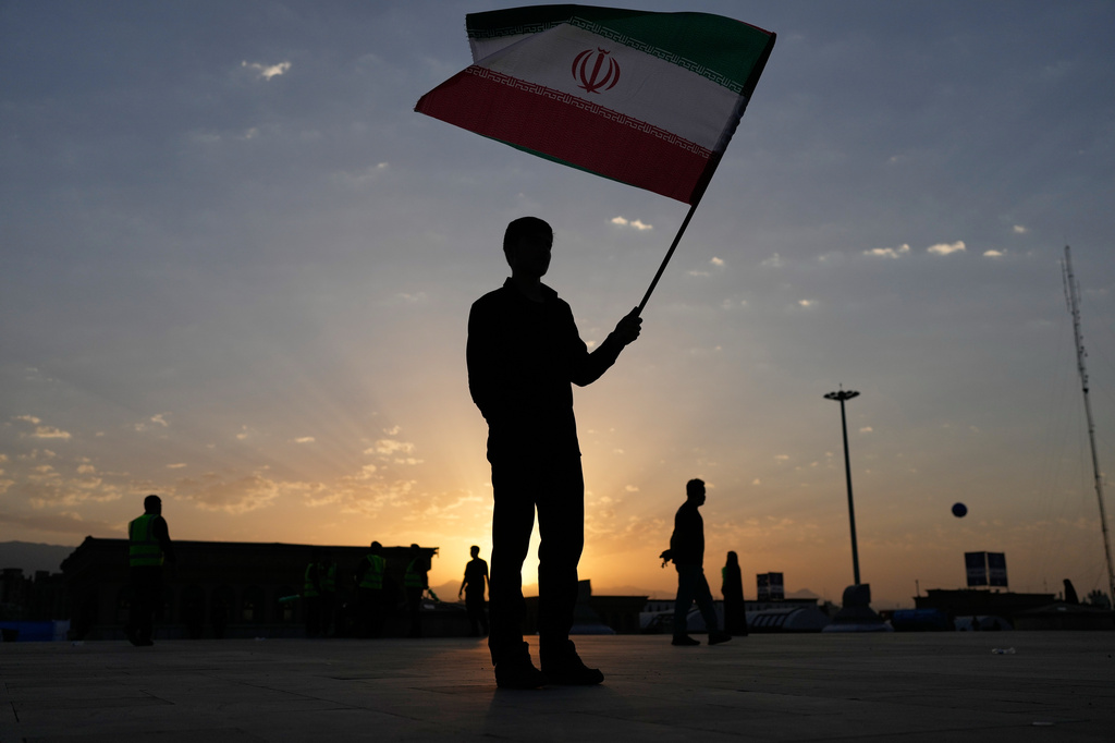 The sun rises as a man holds an Iranian flag on the esplanade of the Imam Khomeini Mosalla Grand Mosque before the start of the dayslong funeral ceremonies for the late Iranian Supreme Leader Ayatollah Ali Khamenei and members of his family in Tehran, Iran, Saturday, July 4, 2026. (AP Photo/Altaf Qadri)