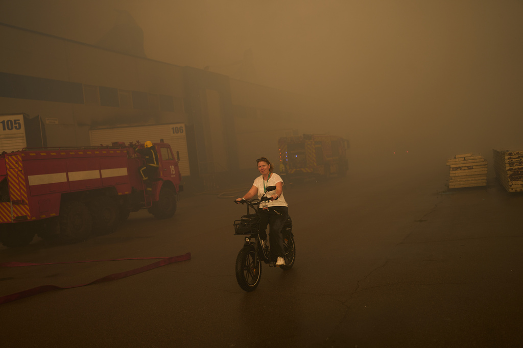 A woman rides a bicycle as firefighters try to extinguish a fire at a destroyed pharmaceutical warehouse following Russian drone attacks on the outskirts of Kyiv, Ukraine, Thursday, Sept. 3, 2026. (AP Photo/Francisco Seco)