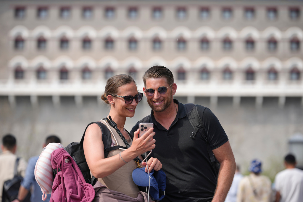 Foreign tourists pose for a selfie as they stroll along the Qianmen pedestrian shopping street, in Beijing, Sunday, April 12, 2026. (AP Photo/Andy Wong)