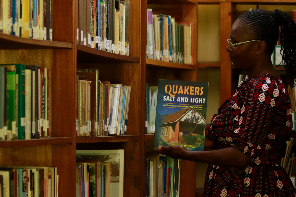 Linet Mmbone, an assistant librarian at the Friends Theological College holding out a book from the shelf, in Kaimosi, Kenya, Saturday, Sept. 19, 2026. (AP Photo/Jackson Njehia)