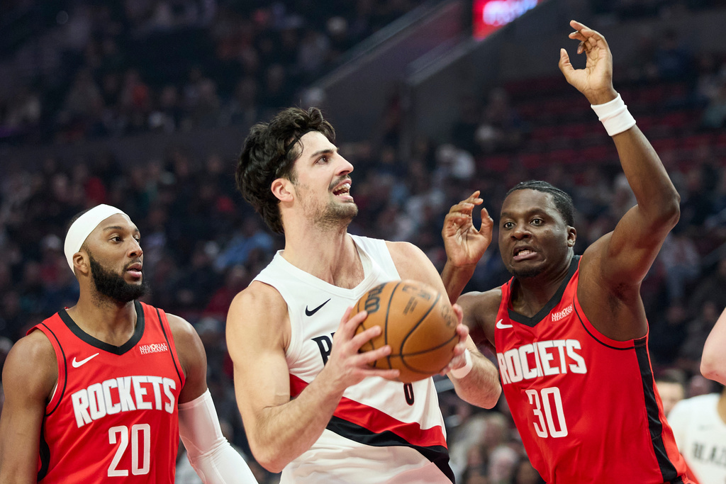 Portland Trail Blazers forward Deni Avdija, center, drives to the basket between Houston Rockets center Clint Capela, right, and guard Josh Okogie during the first half of an NBA basketball game in Portland, Ore., Wednesday, Jan. 7, 2026. (AP Photo/Craig Mitchelldyer)