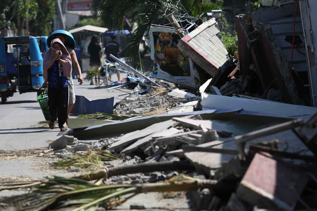 Residents walk past debris from a damaged building in General Santos, southern Philippines, Thursday, June 11, 2026, following Monday's powerful earthquake. (AP Photo/Basilio Sepe)