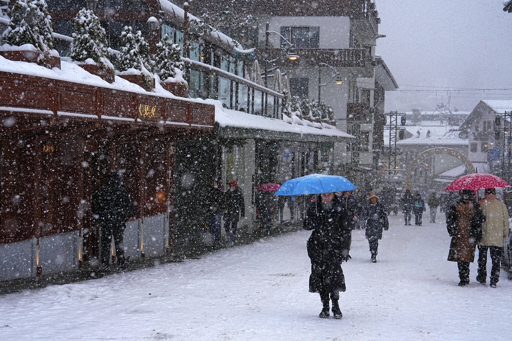 People walk along a main shopping street as snow falls ahead of the 2026 Winter Olympics, in Cortina d'Ampezzo, Italy, Tuesday, Feb. 3, 2026. (AP Photo/Fatima Shbair)