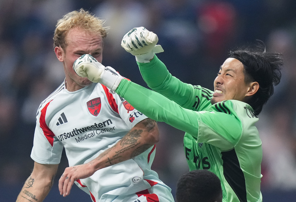 Vancouver Whitecaps goalkeeper Yohei Takaoka, right, follows through after punching the ball away from FC Dallas' Samuel Sarver, left, during the first half of an MLS soccer match in Vancouver, British Columbia, Saturday, Oct. 18, 2025. (Darryl Dyck/The Canadian Press via AP)