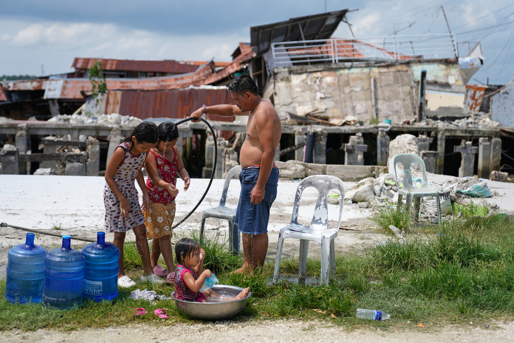 A man takes a bath with his daughters beside damaged structures due to a recent strong earthquake in Bogo, Cebu Province, Central Philippines on Friday, Oct. 3, 2025. (AP Photo/Aaron Favila)