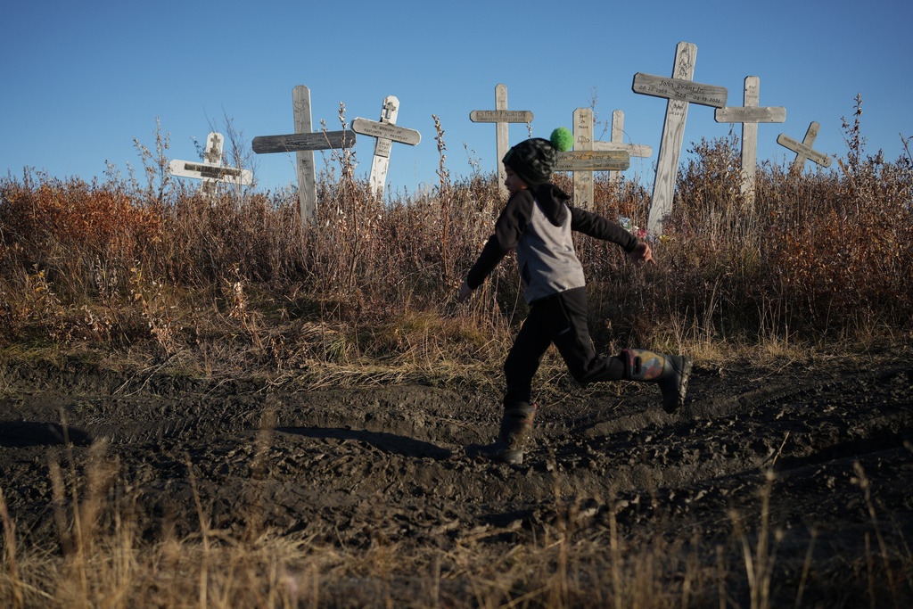 James Schaeffer, 7, runs through a cemetery where thawing permafrost has caused grave markers to tilt and the ground to warp in Kotzebue, Alaska, Friday, Sept. 26, 2025. (AP Photo/Annika Hammerschlag)