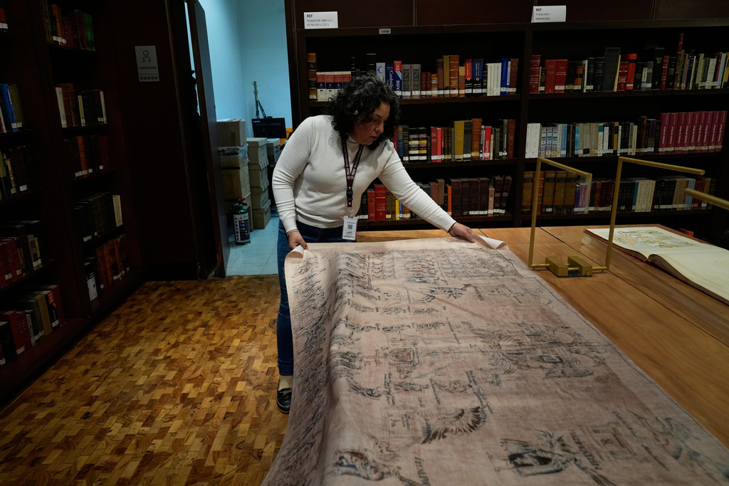 Areli Ortiz, technical deputy director of the National Institute of Anthropology and History, shows a fabric featuring images of La Malinche and Hernan Cortes from a facsimile of part of the 16th century Tlaxcala Codex in Mexico City, Wednesday, Oct. 8, 2025. (AP Photo/Marco Ugarte)