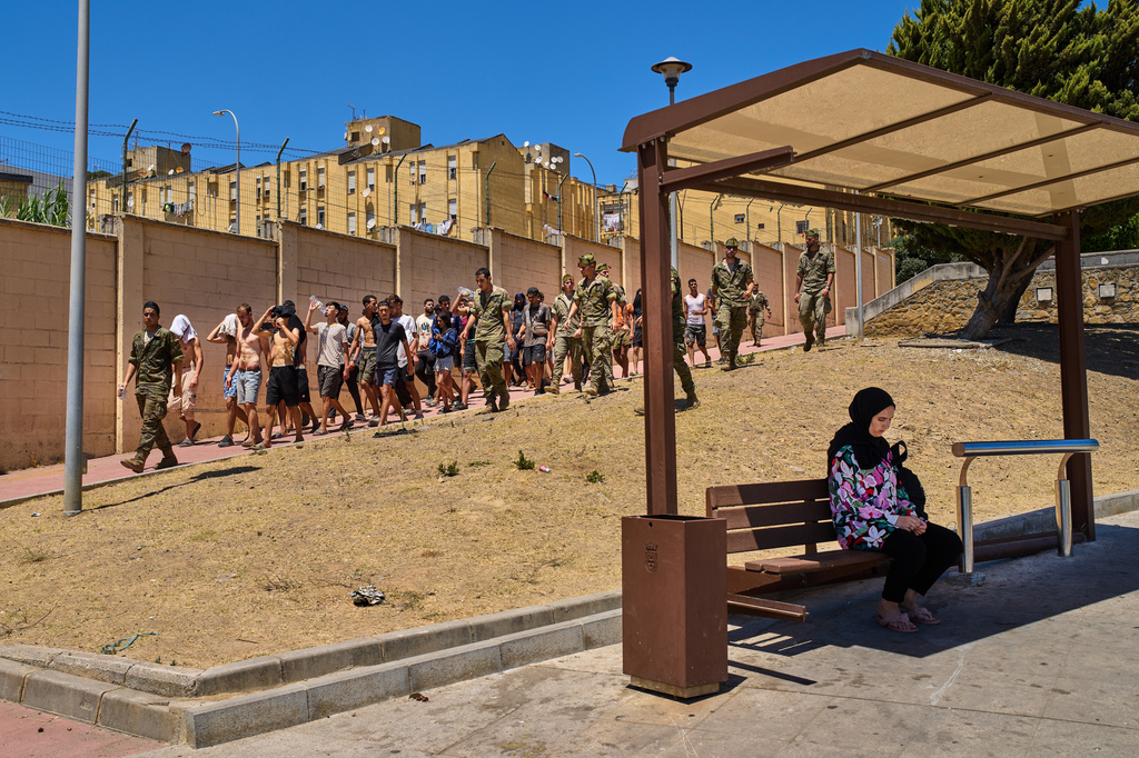A Ceuta resident sits at a bus station as migrants who crossed into Spain are escorted by Spanish soldiers toward the Spanish-Moroccan border, for their return to Morocco from the Spanish enclave of Ceuta, Sunday, Aug. 2, 2026. (AP Photo/Bernat Armangue)