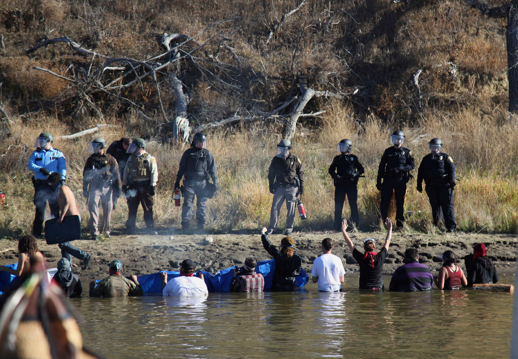 FILE - In this Nov. 2, 2016 file photo, protesters demonstrating against the expansion of the Dakota Access Pipeline wade in cold creek waters confronting local police as remnants of pepper spray waft over the crowd near Cannon Ball, N.D. (AP Photo/John L. Mone, File)