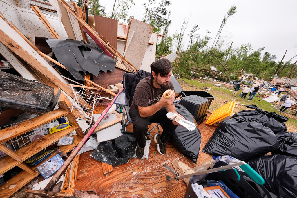 Logan Branch eats a hotdog as he sits among the debris of what is left of his home at Gene's Mobile Home Supply, a trailer park in Bogue Chitto, Miss., Thursday, May, 7, 2026, after a tornado cut across the state. (AP Photo/Gerald Herbert)