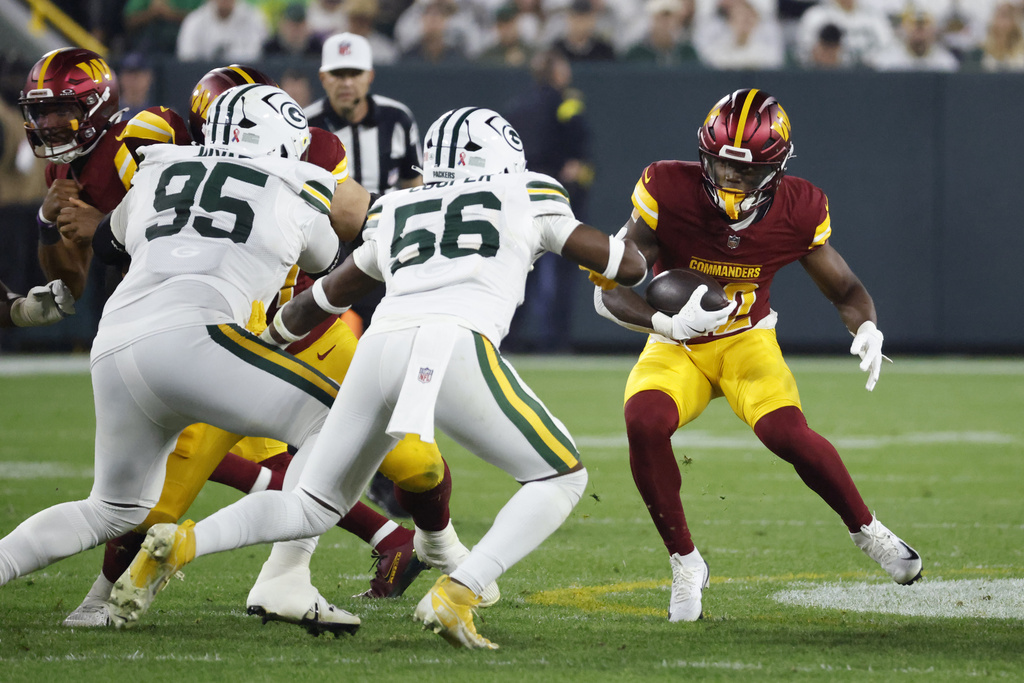 Washington Commanders running back Jacory Croskey-Merritt, right, runs with the ball as Green Bay Packers linebacker Edgerrin Cooper (56) and defensive lineman Devonte Wyatt (95) defend during the second half of an NFL football game Thursday, Sept. 11, 2025, in Green Bay, Wis. (AP Photo/Mike Roemer)