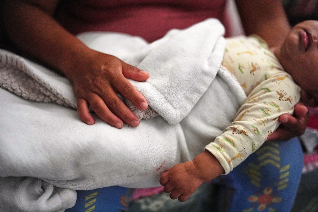 Guatemalan migrant Amavilia, 31, holds her infant son, whose father Edgar was detained days after his birth and later deported to Guatemala, inside the South Florida apartment where she lives with her two children and a roommate, Wednesday, Oct. 8, 2025. (AP Photo/Rebecca Blackwell)