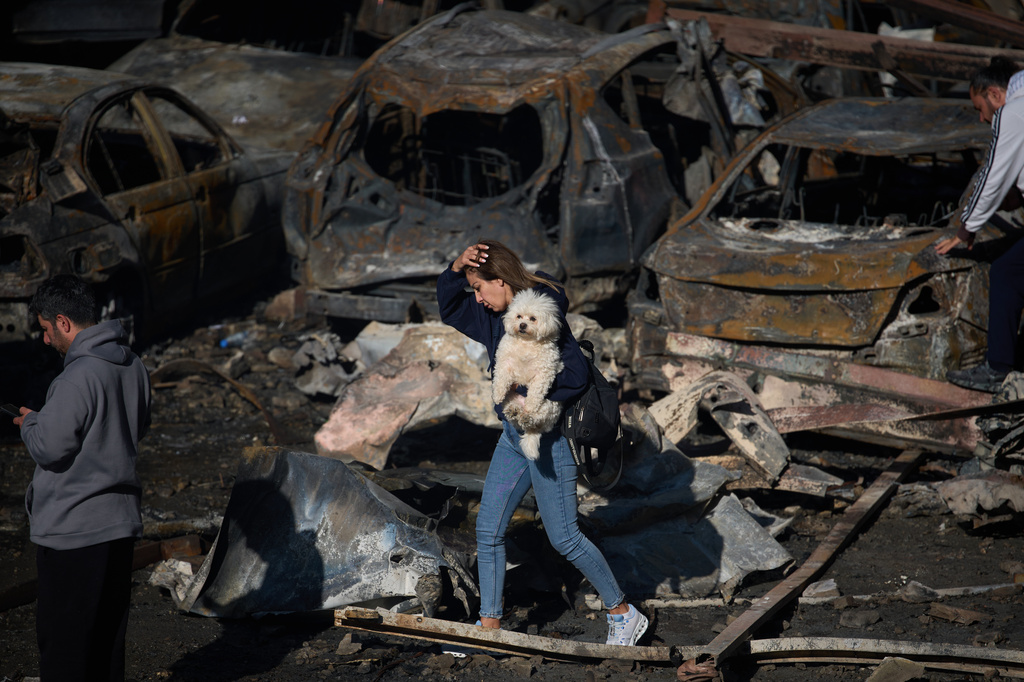 A woman holds her dog as she walks past burned cars a day after an Israeli airstrike in Beirut, Lebanon, Thursday, April 9, 2026. (AP Photo/Emilio Morenatti)