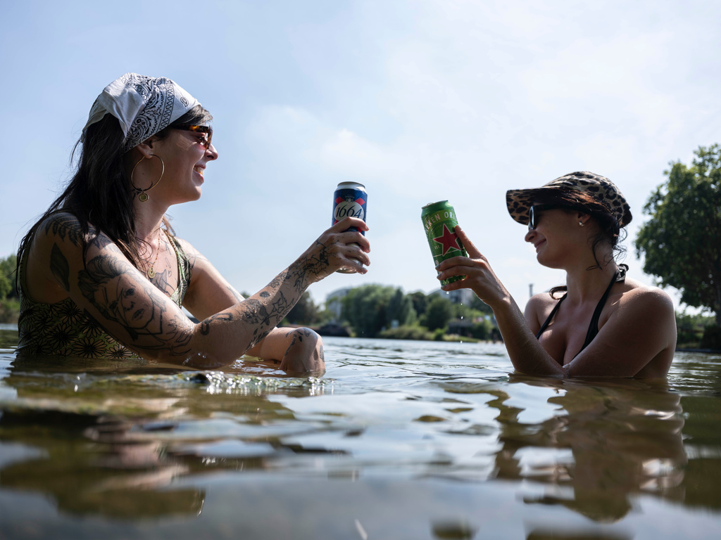 Two women take a drink into a river in Lille, northern France, Monday June 22, 2026. (AP Photo/Jean-Francois Badias)