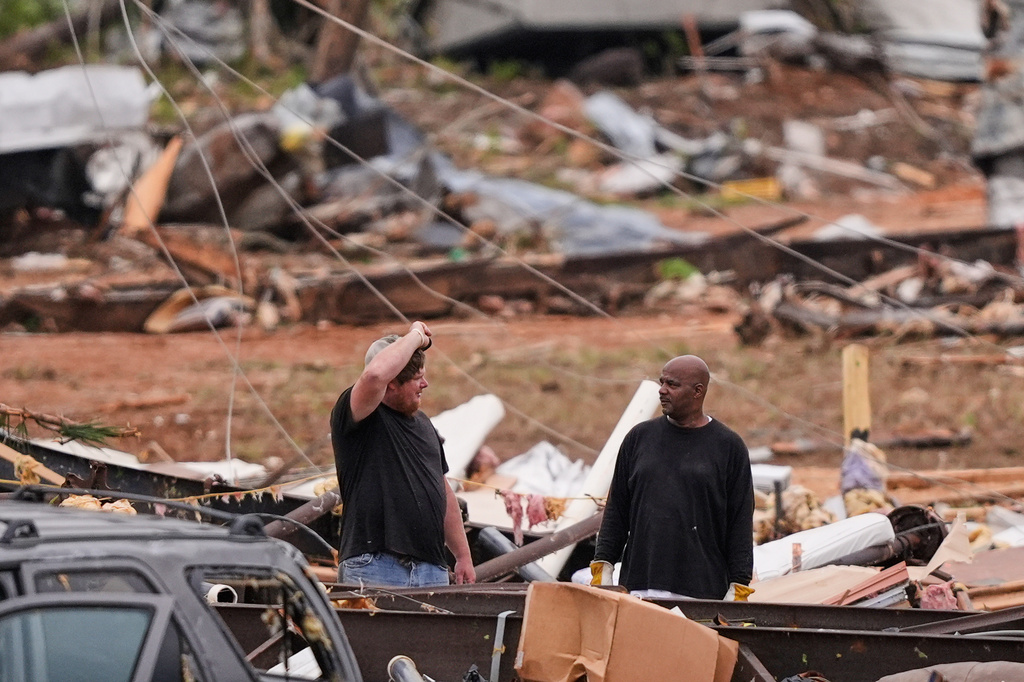 People stand among debris at Gene's Mobile Home Supply, a trailer park in Bogue Chitto, Miss., Thursday, May, 7, 2026, after a tornado cut across the state. (AP Photo/Gerald Herbert)