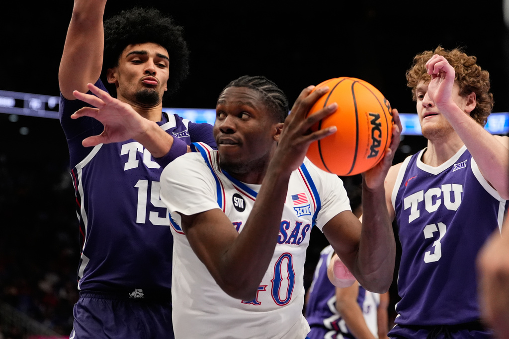 Kansas' Flory Bidunga, center, looks past TCU's David Punch, left, as TCU's Liutauras Lelevicius (3) watches during the second half of an NCAA college basketball game in the quarterfinal round of the Big 12 Conference tournament Thursday, March 12, 2026, in Kansas City, Mo. (AP Photo/Charlie Riedel)