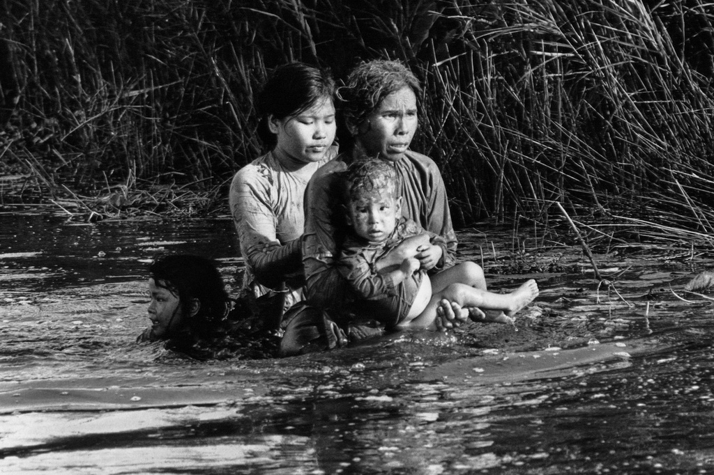 FILE - A Vietnamese woman and three children wade through a swamp after government troops fired into their hamlet less than 150 miles southeast of Saigon, Vietnam, on Aug. 30, 1966. (AP Photo/Dang Van Phuoc, File)