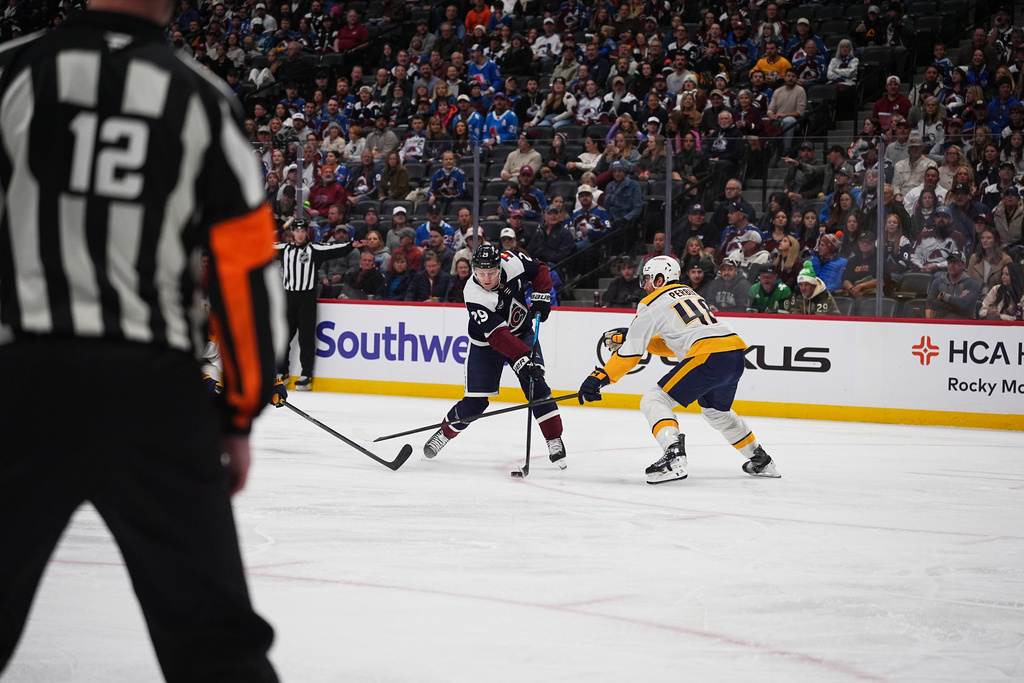 Colorado Avalanche center Nathan MacKinnon, left, shoots the puck past Nashville Predators defenseman Nick Perbix for a goal in the first period of an NHL hockey game, Saturday, Dec. 13, 2025, in Denver. (AP Photo/David Zalubowski)
