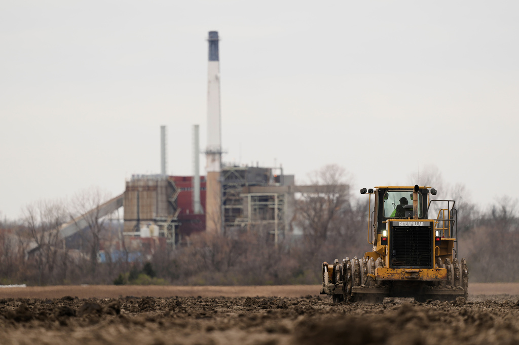 FILE - A worker prepares a plot of land for an AI data center, with a retired power plant being refurbished to provide electricity for the facility in the distance, March 24, 2026, in Independence, Mo. (AP Photo/Charlie Riedel, File)