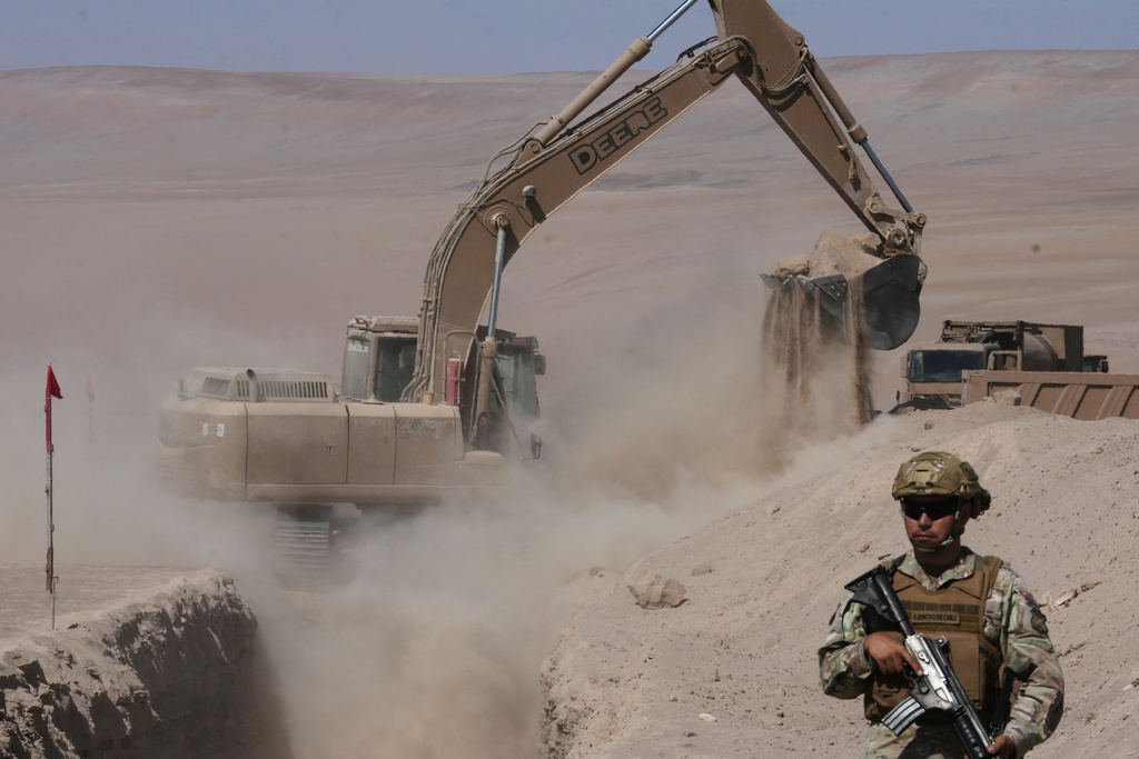 A soldier stands guard where a machine digs as part of measures to deter irregular migration along the northern border at the Chacalluta border crossing, in Arica, Chile, Monday, March 16, 2026. (AP Photo/Esteban Felix)
