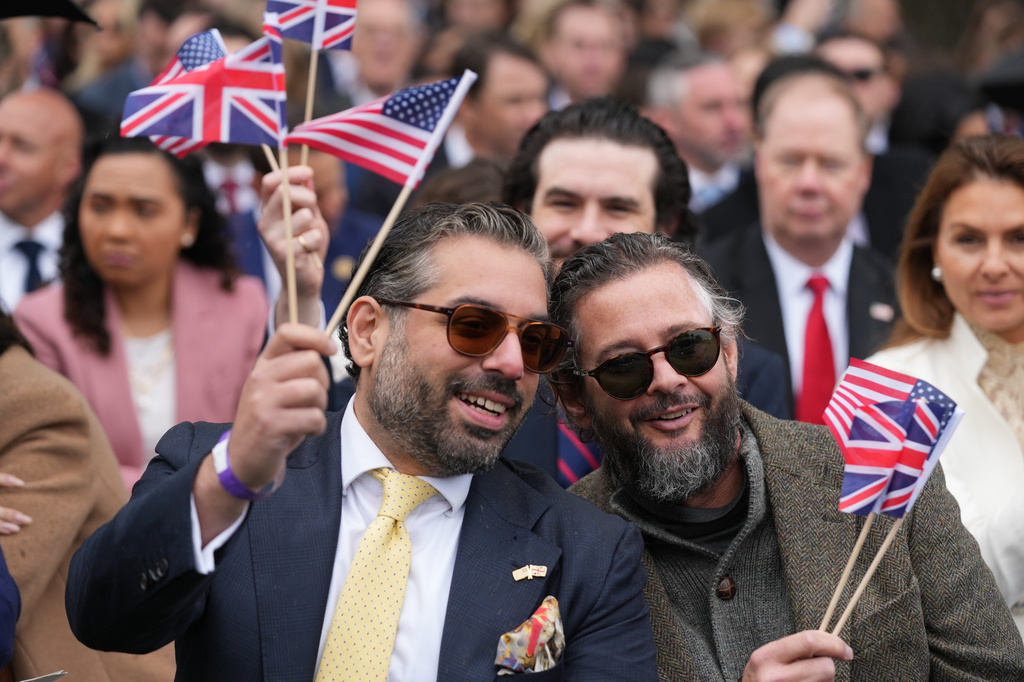 Guests wave flags as they arrive to watch President Donald Trump and first lady Melania Trump greet Britain's King Charles III and Queen Camilla during a State Visit arrival ceremony on the South Lawn of the White House, Tuesday, April 28, 2026, in Washington. (AP Photo/Mark Schiefelbein)