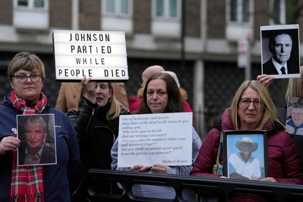FILE - Protesters show pictures of COVID victims and placards outside Dorland House as Britain's former Prime Minister Boris Johnson testifies at Britain's COVID-19 public inquiry in London, on Dec. 7, 2023. (AP Photo/Kirsty Wigglesworth, file)